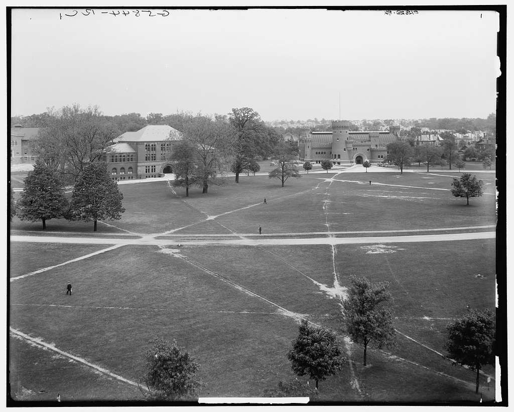 A black and white photo of the OSU oval around 100 years ago with no paved sidewalks and wear patterns in the grass. 